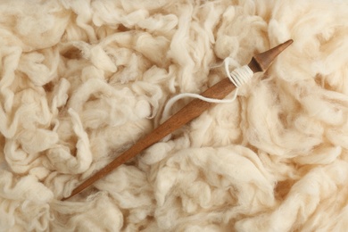 Photo of Soft white wool with spindle as background, top view