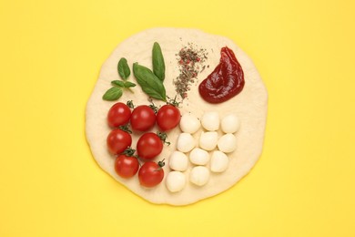 Raw dough and other ingredients for pizza on yellow background, top view