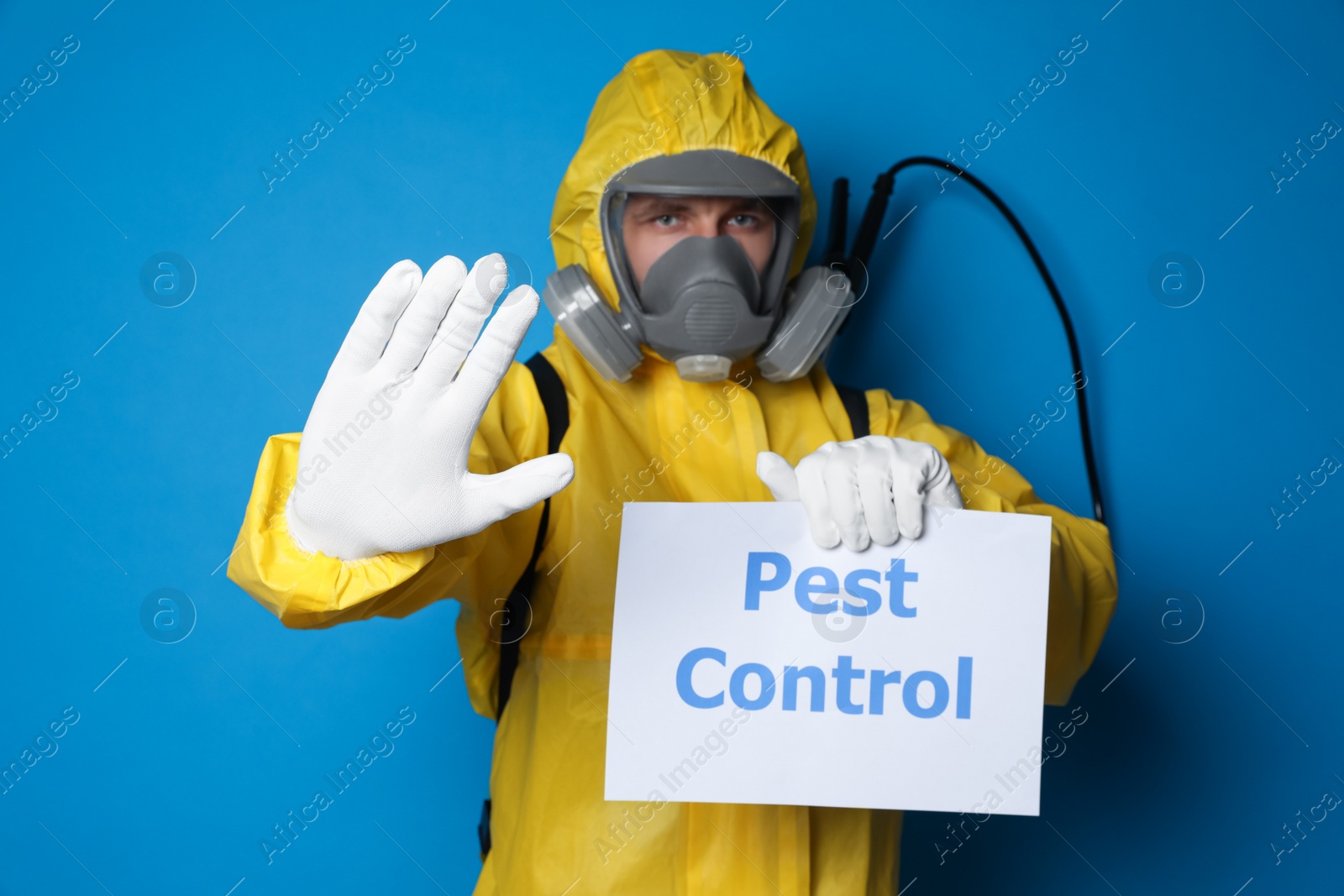 Photo of Man wearing protective suit with insecticide sprayer holding sign PEST CONTROL on blue background