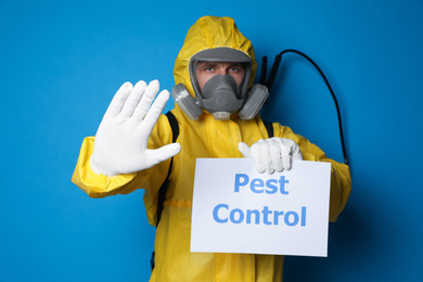 Photo of Man wearing protective suit with insecticide sprayer holding sign PEST CONTROL on blue background