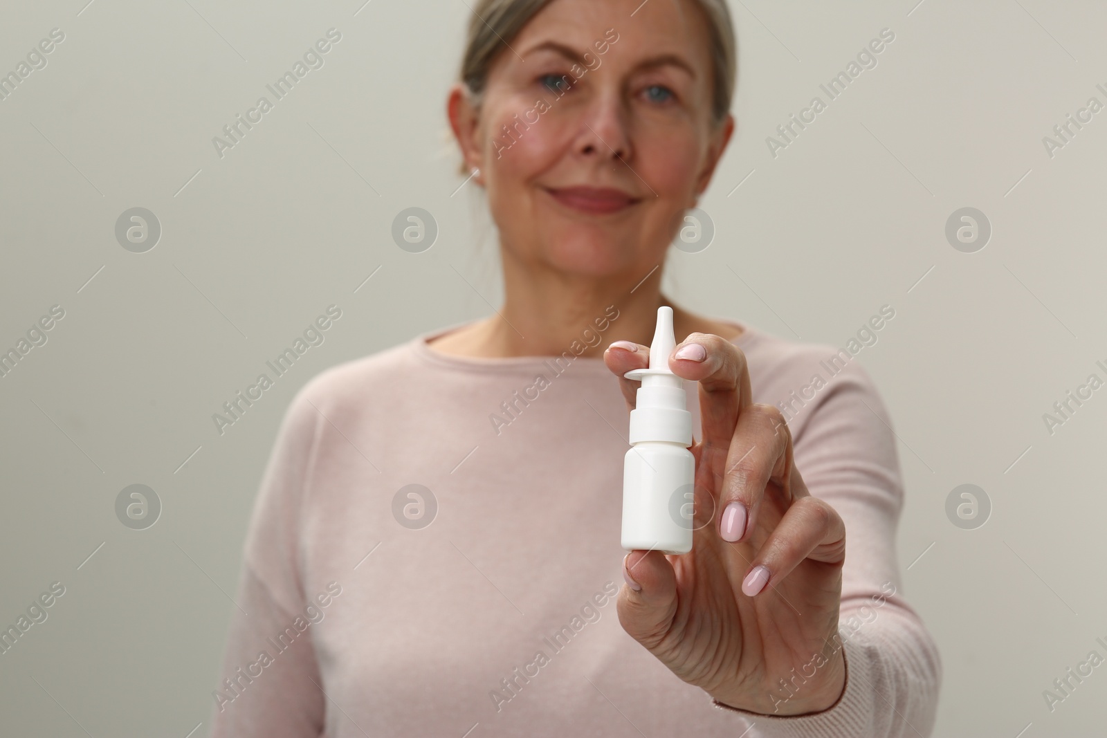 Photo of Woman holding nasal spray on light grey background, focus on bottle