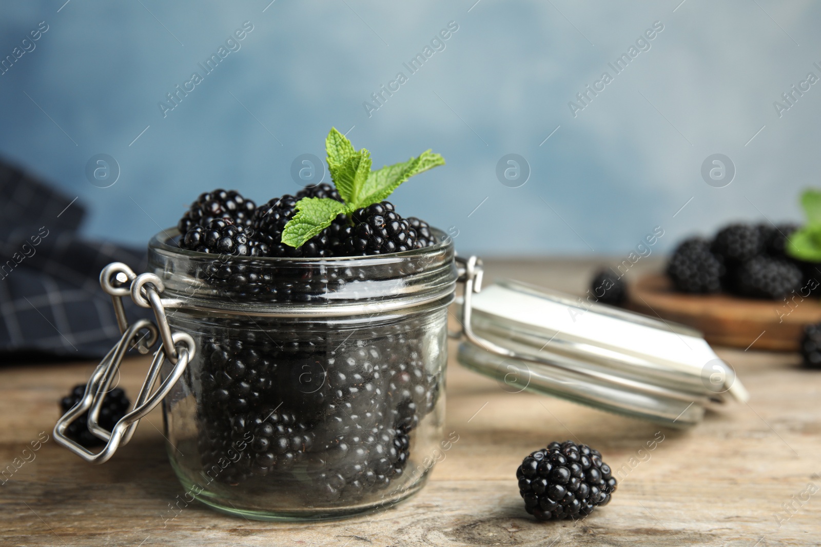 Photo of Glass jar of tasty blackberries and mint on wooden table