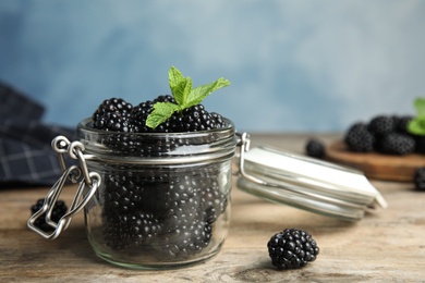 Photo of Glass jar of tasty blackberries and mint on wooden table