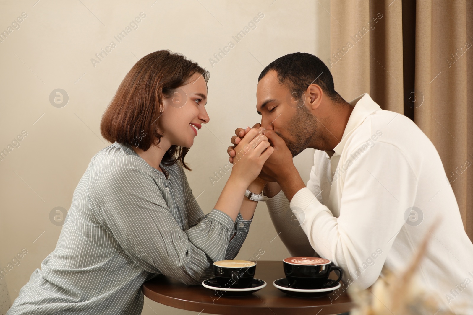 Photo of Romantic date. Guy kissing his girlfriend's hands in cafe