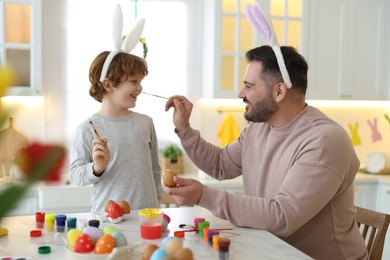 Easter celebration. Father with his little son having fun while painting eggs at white marble table in kitchen
