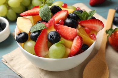 Photo of Tasty fruit salad in bowl, ingredients and spoon on light blue wooden table, closeup