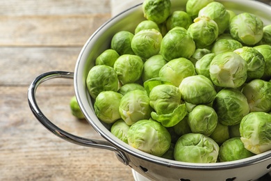 Photo of Colander with Brussels sprouts on wooden background, closeup