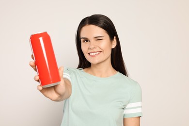 Beautiful young woman holding red tin can with beverage on light grey background