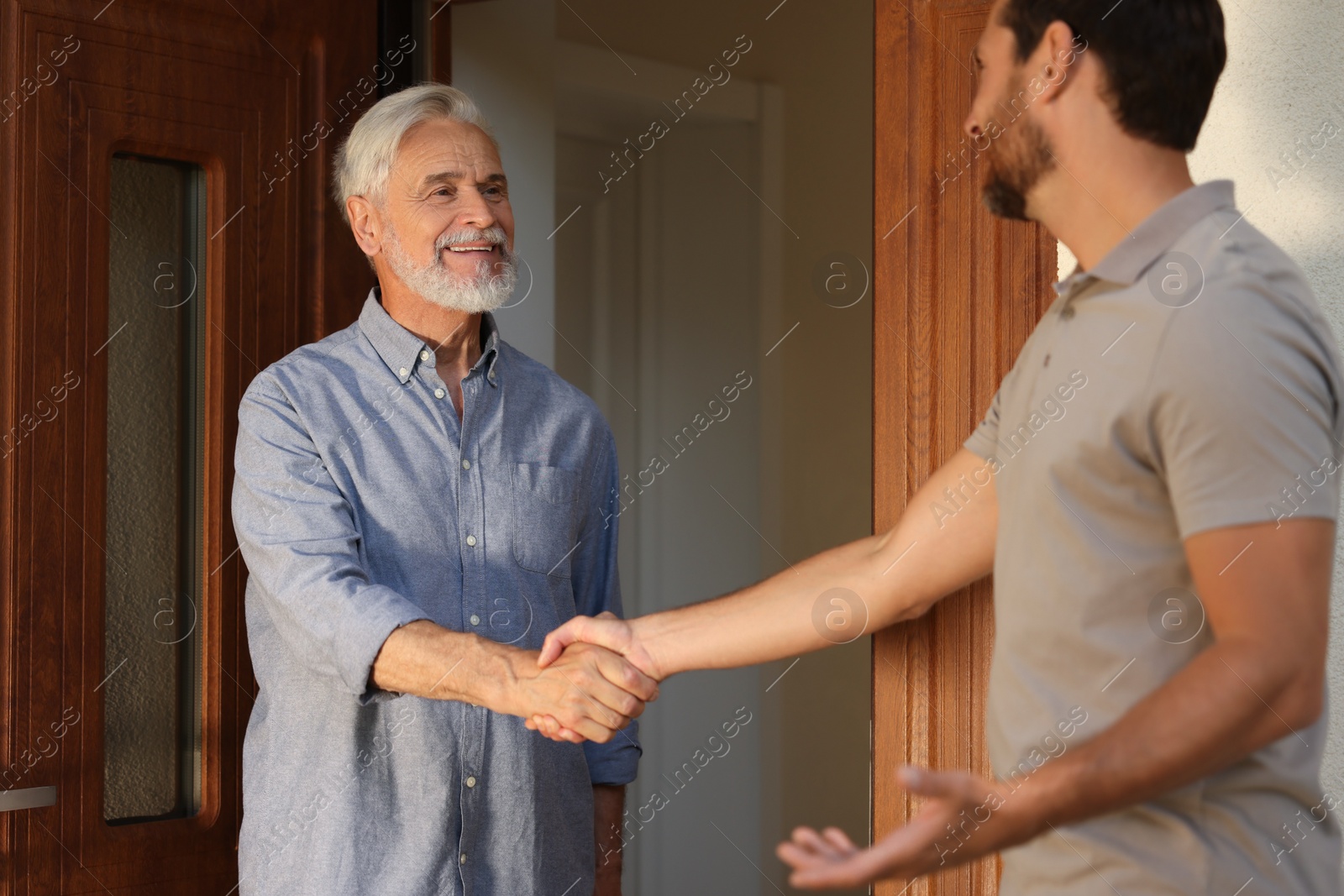 Photo of Friendly relationship with neighbours. Happy men shaking hands near house outdoors