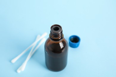 Photo of Bottle of medical iodine and cotton buds on light blue background, closeup