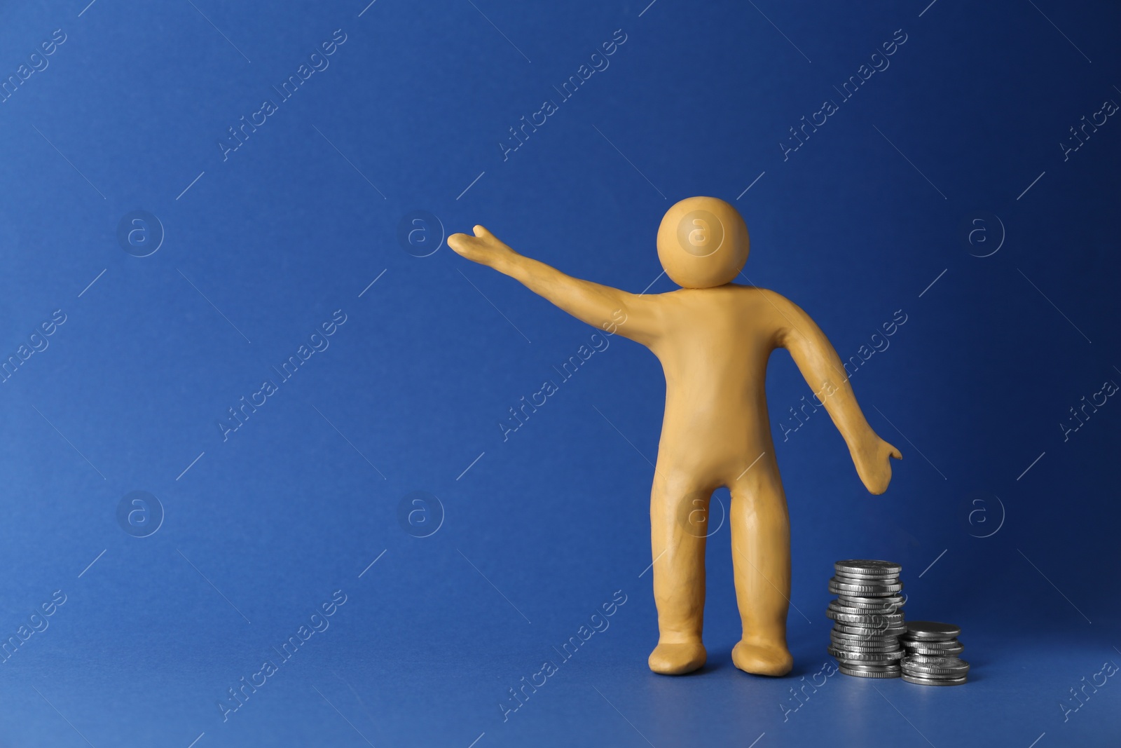Photo of Human figure made of yellow plasticine with stacked coins on blue background. Space for text