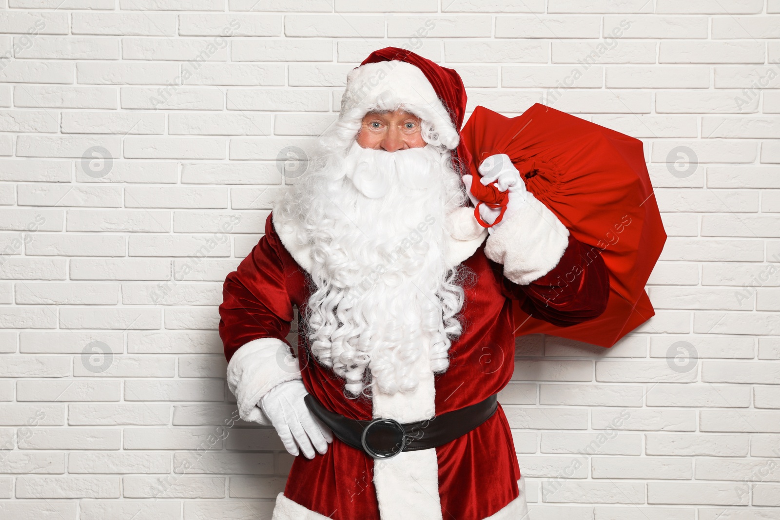 Photo of Authentic Santa Claus with bag full of gifts against white brick wall