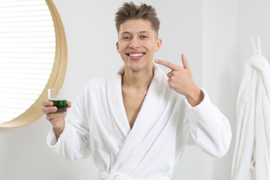 Young man with mouthwash pointing at his healthy teeth in bathroom