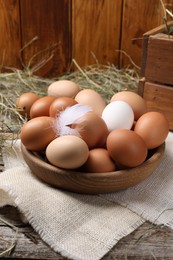 Fresh chicken eggs in bowl and dried hay on wooden table