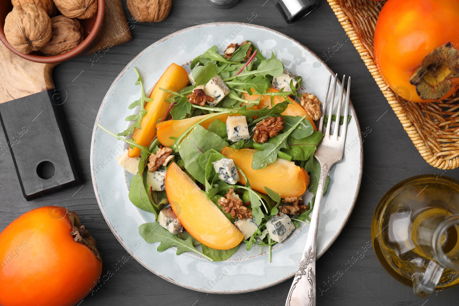 Photo of Tasty salad with persimmon, blue cheese and walnuts served on grey wooden table, flat lay
