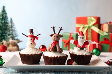 Different beautiful Christmas cupcakes on blue table with festive decor and snow