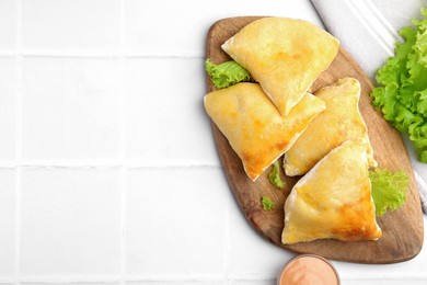 Photo of Delicious samosas with lettuce and sauce on white tiled table, flat lay. Space for text