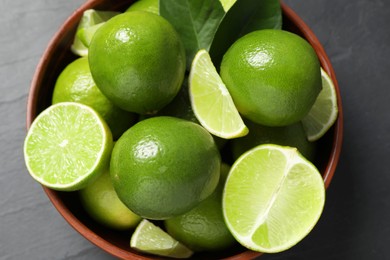 Photo of Fresh ripe limes in bowl on black table, top view
