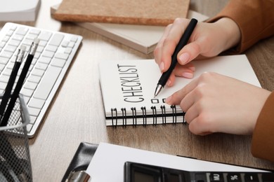 Woman filling Checklist at wooden table, closeup