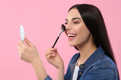 Photo of Beautiful woman with cosmetic pocket mirror applying makeup on pink background