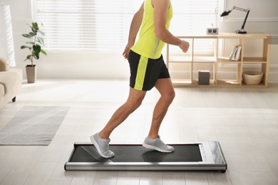 Photo of Sporty man training on walking treadmill at home, closeup