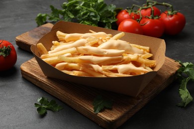 Photo of Tasty potato fries, cheese sauce in paper container and products on black table, closeup