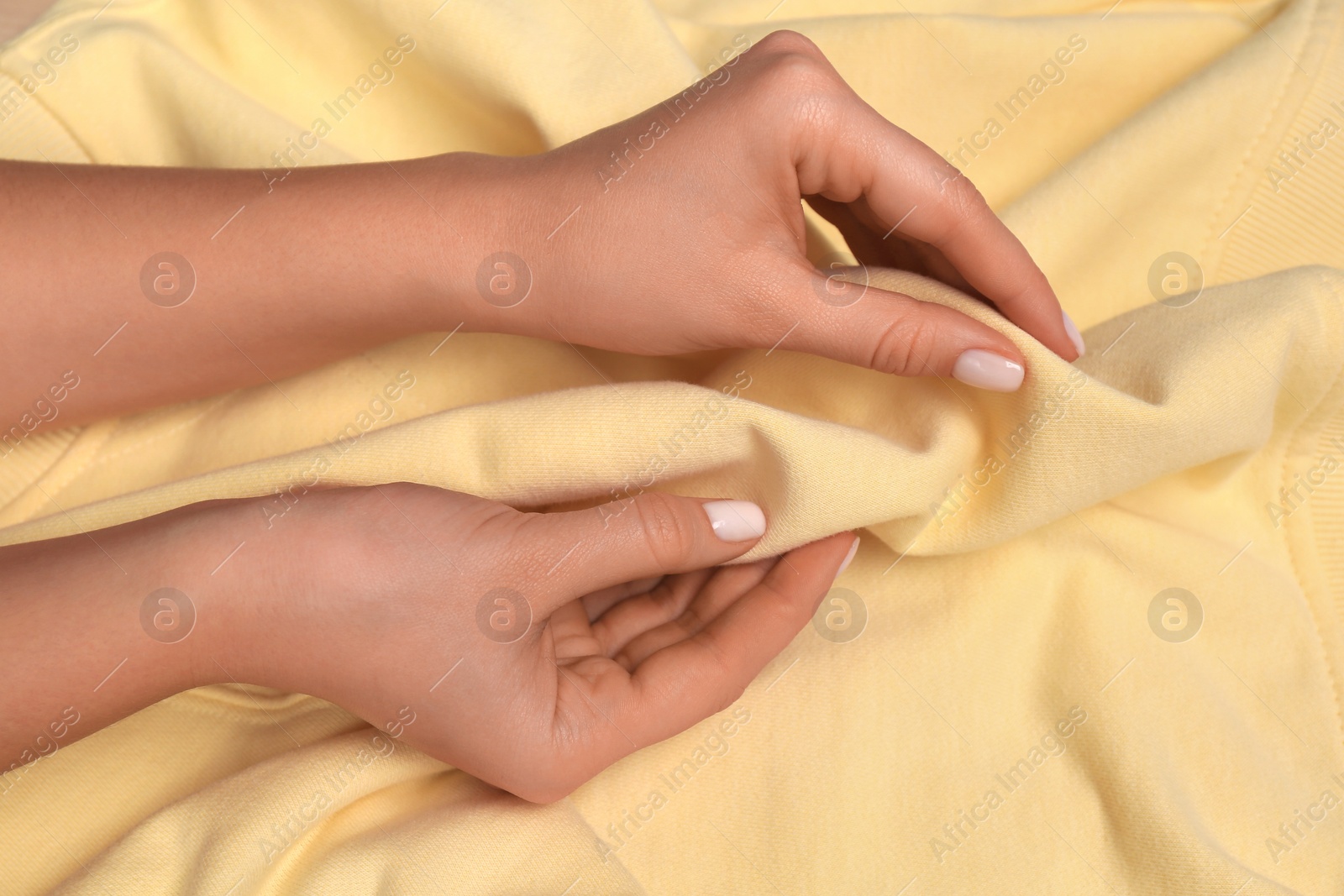 Photo of Woman touching soft yellow fabric, closeup view