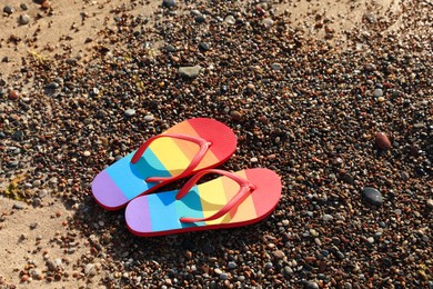 Photo of Stylish rainbow flip flops on pebbles at beach, above view