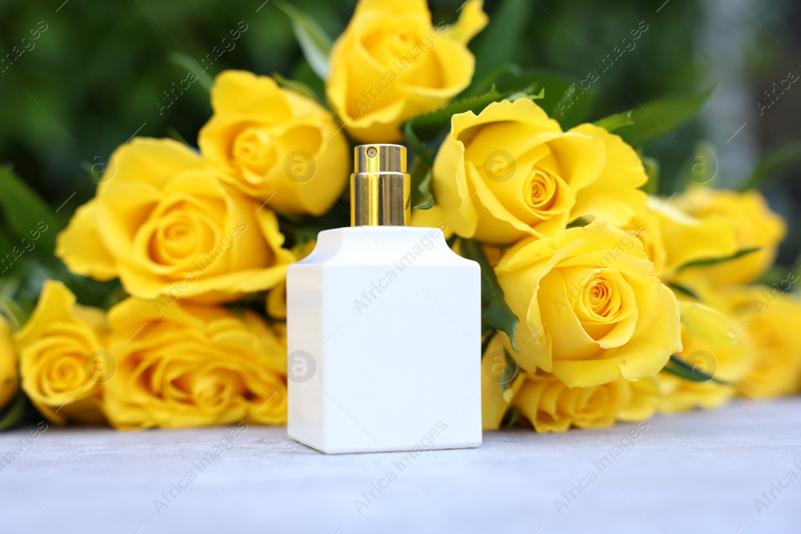 Photo of Perfume and beautiful bouquet of yellow roses on light table