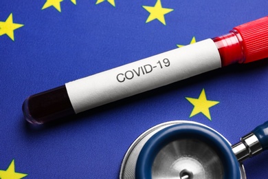 Photo of Stethoscope and test tube with blood sample on European Union flag background, closeup. Coronavirus outbreak