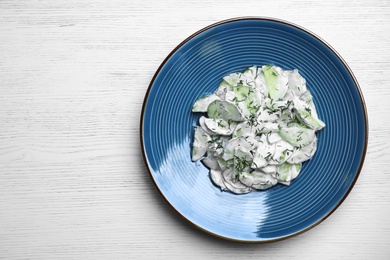 Plate of creamy cucumber salad on white wooden background, top view. Space for text