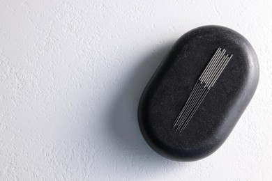 Photo of Acupuncture needles and spa stone on white table, top view. Space for text