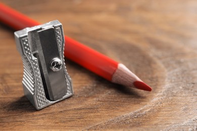 Photo of Metal sharpener and red pencil on wooden table, closeup. Space for text