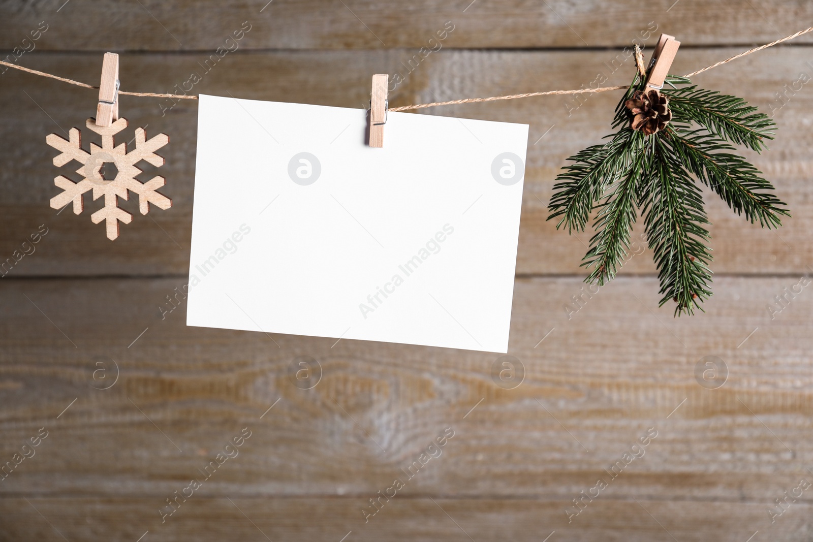 Photo of Blank Christmas card and festive decor on rope against wooden background. Space for text