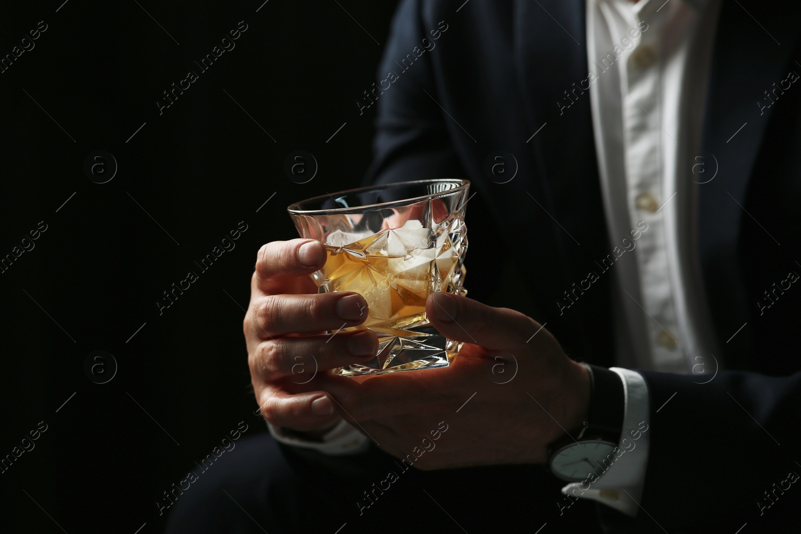 Photo of Man holding glass of whiskey with ice cubes on black background, closeup