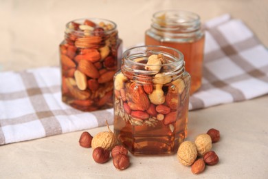 Jars with different nuts and honey on beige table