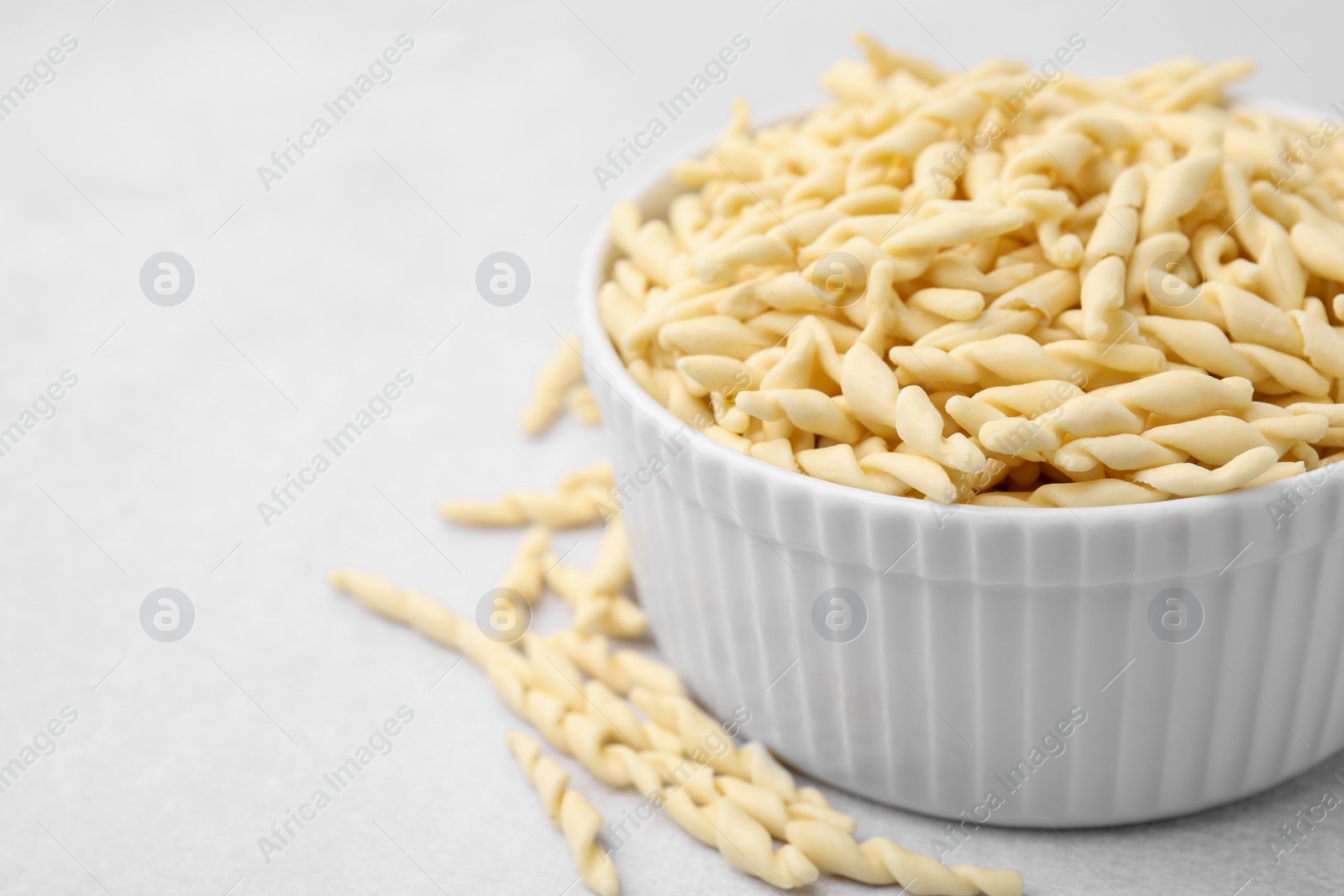 Photo of Bowl with uncooked trofie pasta on light grey table, closeup. Space for text