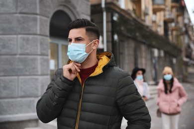 Man putting on medical face mask while walking outdoors. Personal protection during COVID-19 pandemic