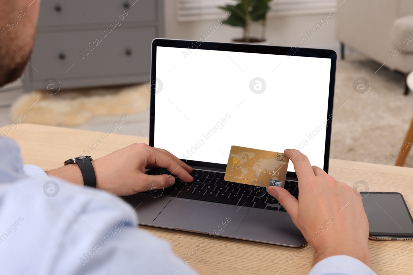 Photo of Man with credit card using laptop for online shopping at wooden table indoors, closeup