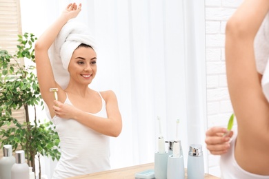 Photo of Beautiful young woman shaving armpit at home