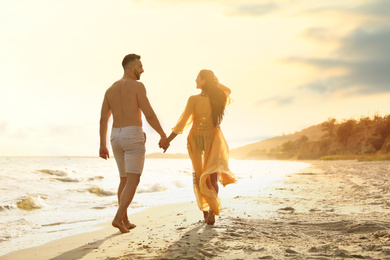 Photo of Happy couple walking together on beach at sunset, back view