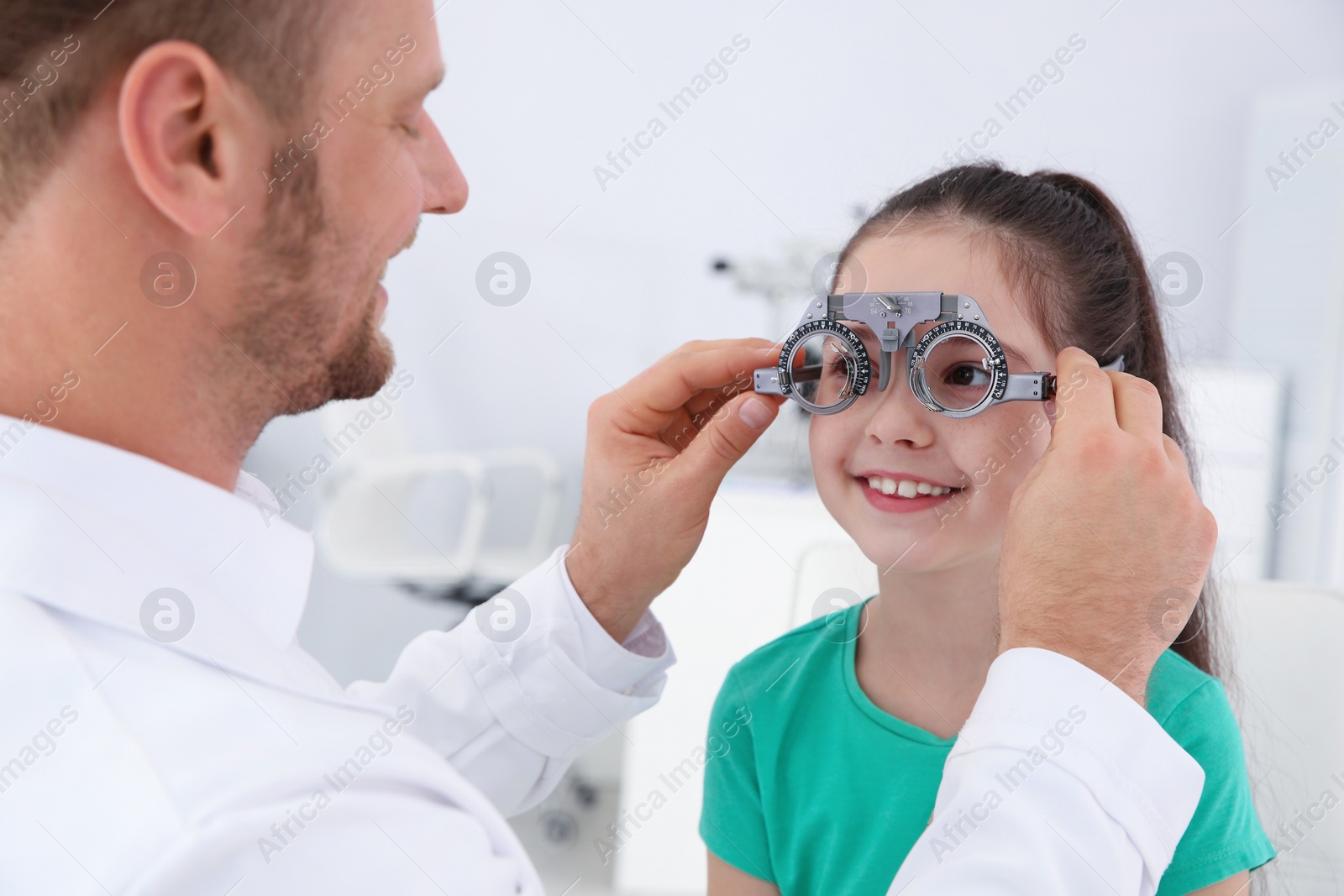 Photo of Children's doctor putting trial frame on little girl in clinic. Eye examination