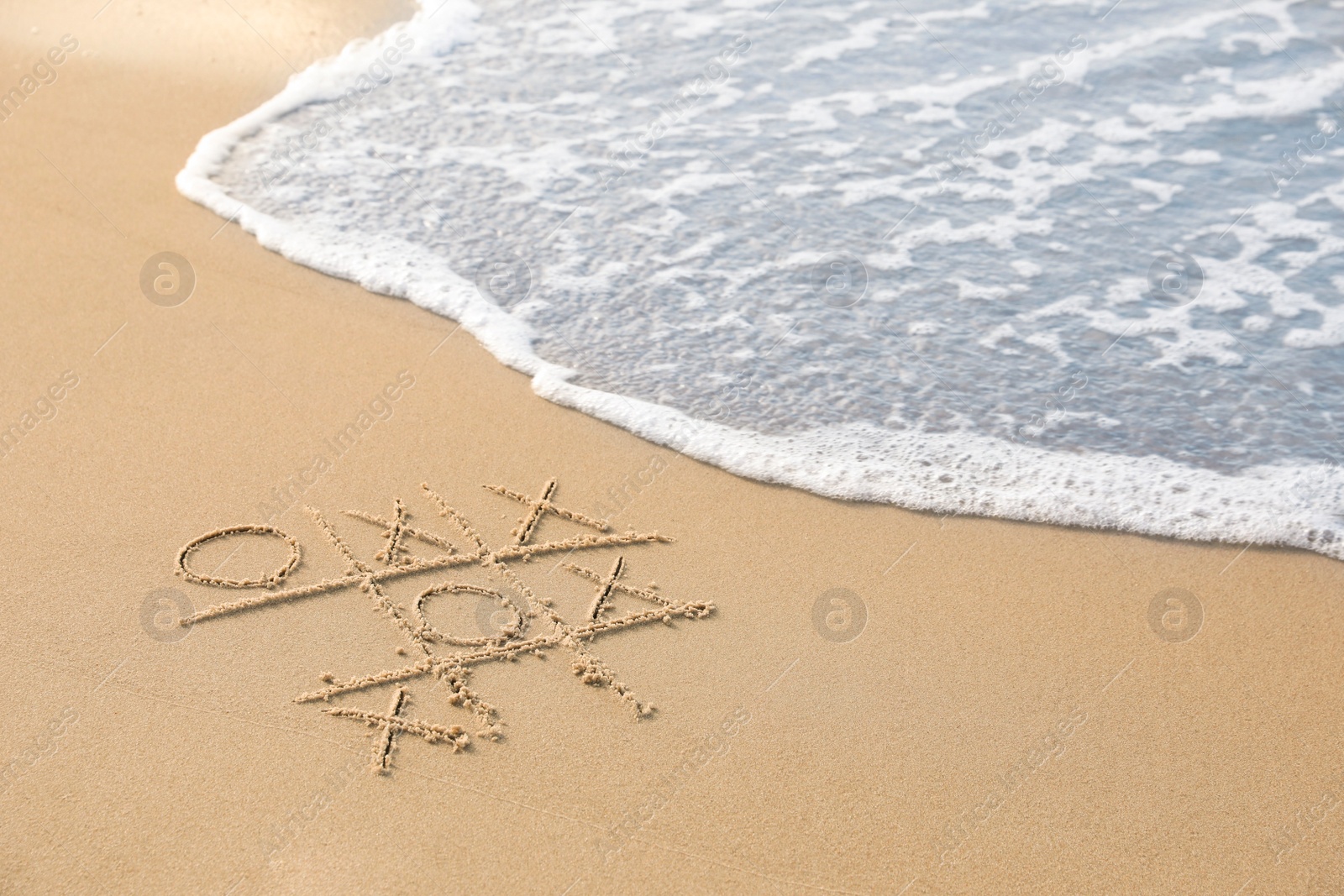 Photo of Tic tac toe game drawn on sand near sea, space for text