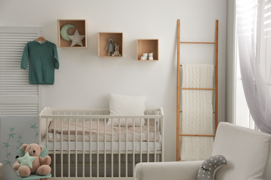 Stylish baby room interior with crib and armchair