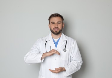 Photo of Young doctor holding something on light grey background