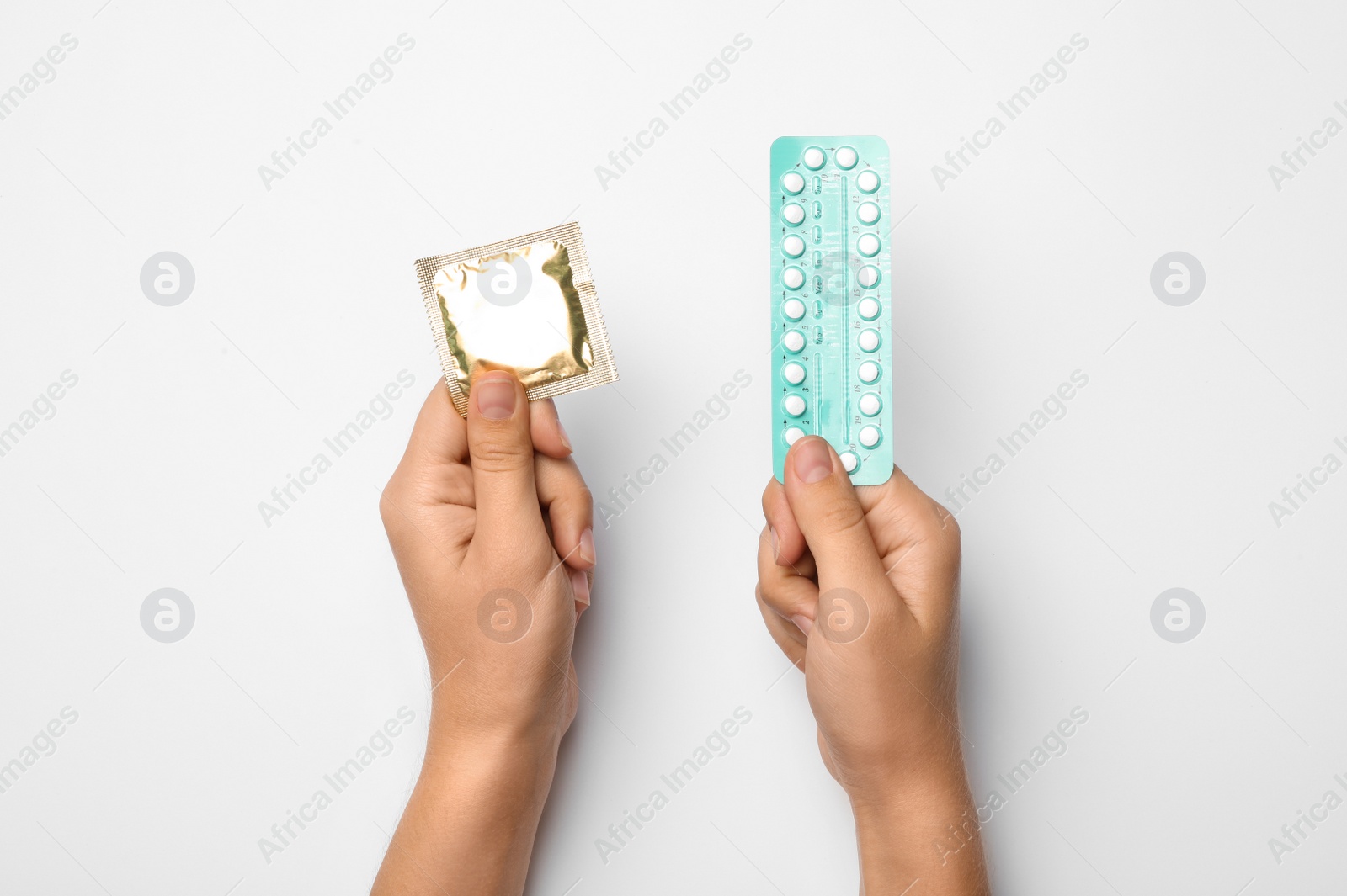 Photo of Woman holding condom and birth control pills on white background, top view. Safe sex