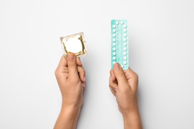 Photo of Woman holding condom and birth control pills on white background, top view. Safe sex