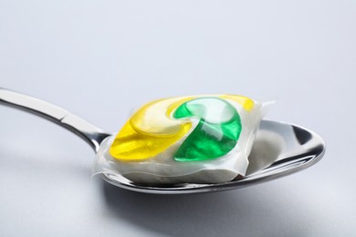 Photo of Spoon with dishwasher detergent pod on light background, closeup