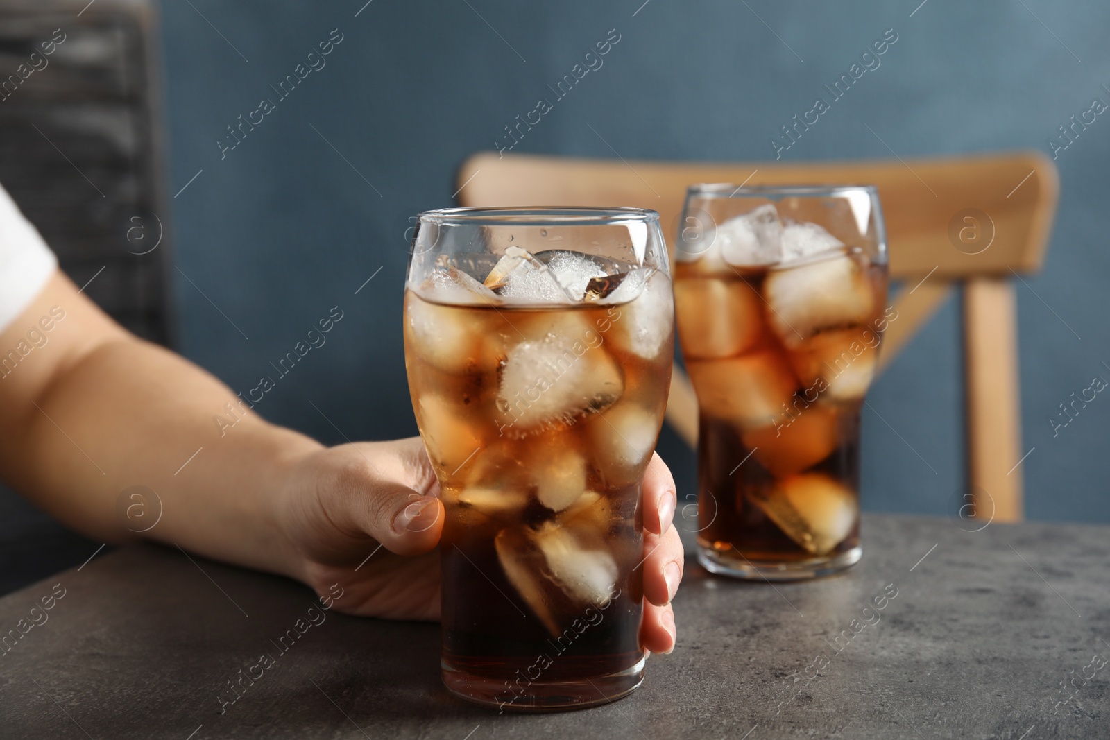 Photo of Woman with glass of tasty refreshing cola at table, closeup view