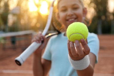 Photo of Cute little girl with tennis racket outdoors, focus on ball